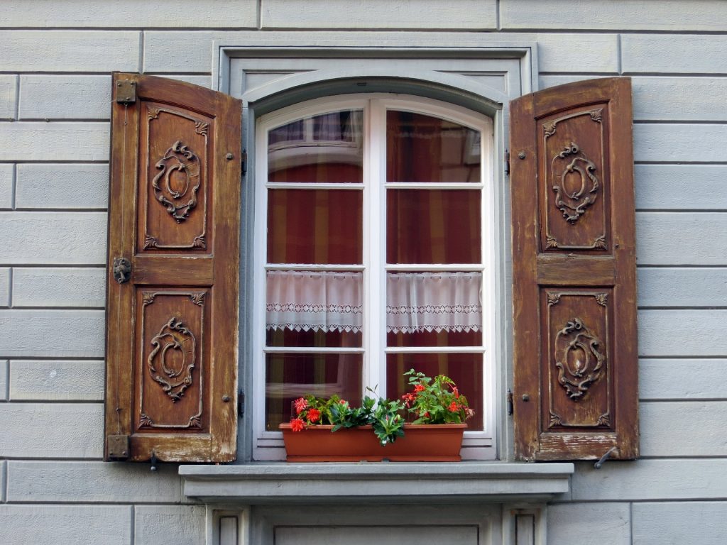 Klassiska träfönster med spröjs och dekorativa fönsterluckor av trä.